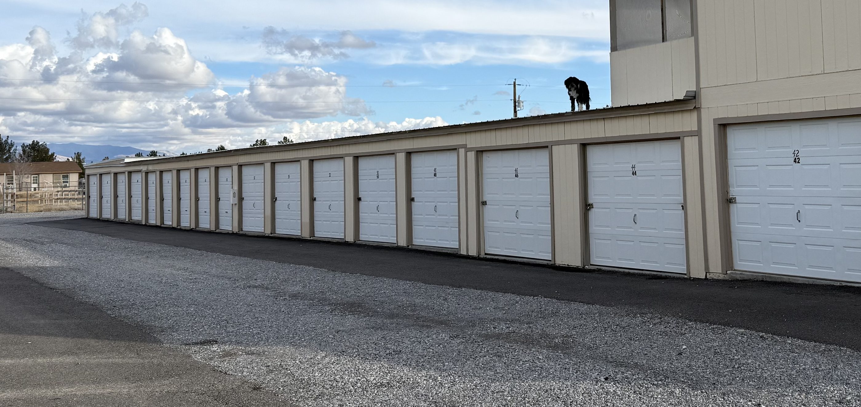Closed white roll-up doors along the paved drive lane at Decroff Storage Units in Pahrump.